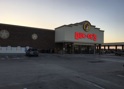 A Buc-ee's convenience store at dusk, featuring a large sign and a parking lot with a few vehicles.