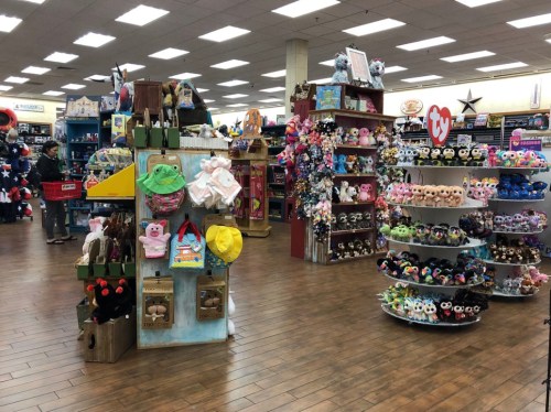 A colorful toy store interior featuring shelves of plush toys and stuffed animals, with wooden flooring and bright lighting.