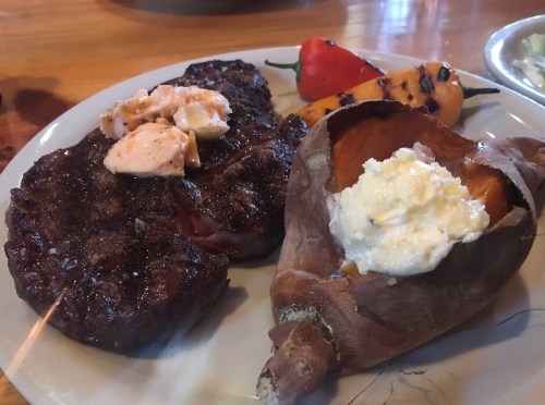 A plate featuring grilled steak with butter, grilled peppers, and a baked sweet potato topped with cream.