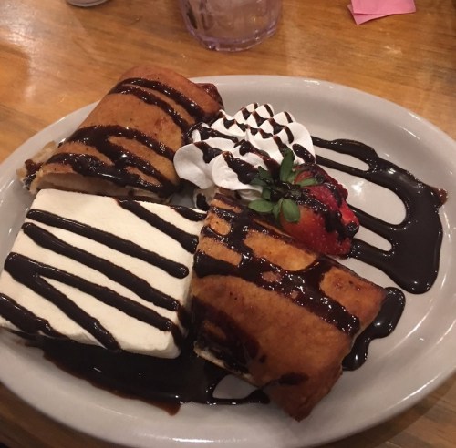 A plate of dessert featuring chocolate-drizzled fried pastries, whipped cream, and a strawberry.