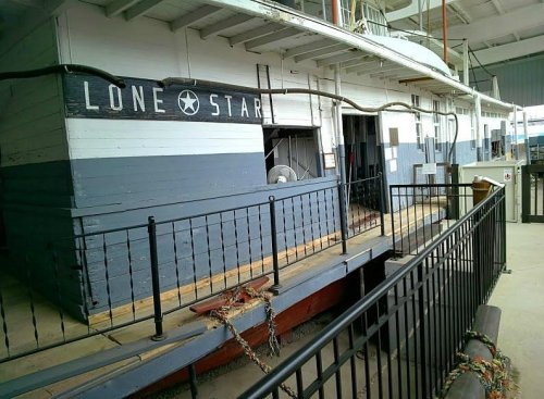 A historic boat named "Lone Star" docked at a marina, featuring a blue and white exterior and a railing in the foreground.