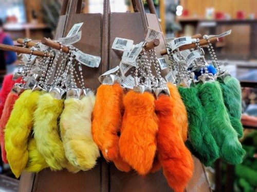 A display of colorful furry keychains in yellow, orange, green, and red hanging from a wooden rack.