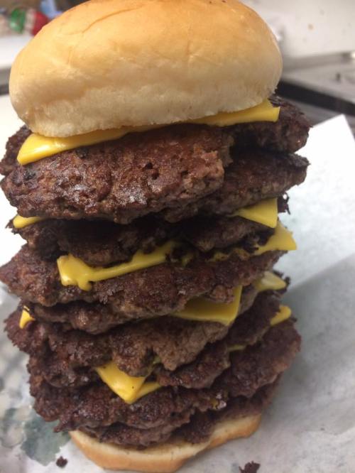 A towering stack of cheeseburgers with multiple beef patties and melted cheese, topped with a bun.