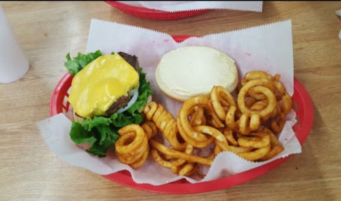 A cheeseburger with lettuce and a bun, served with curly fries on a red tray.
