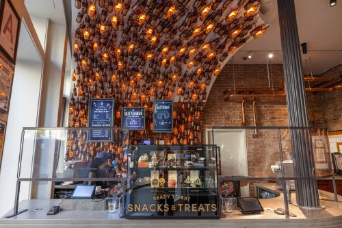 A modern café interior with a unique bottle display, featuring a counter with snacks and treats for sale.