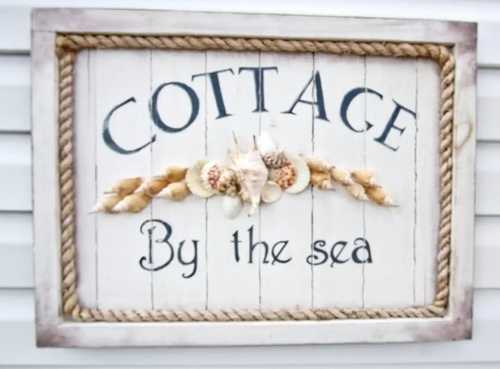 A decorative sign reading "Cottage By the Sea," adorned with seashells and rope accents.