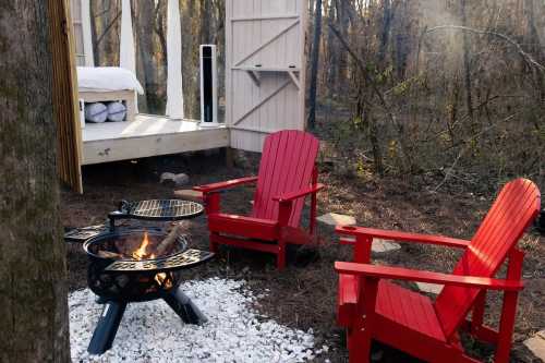 Cozy outdoor seating with red chairs around a fire pit, surrounded by trees and a cabin in the background.