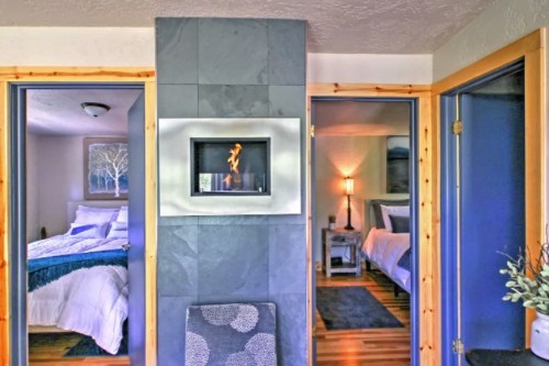 A cozy interior view showing two rooms with a modern fireplace in the center, framed by wooden doors.
