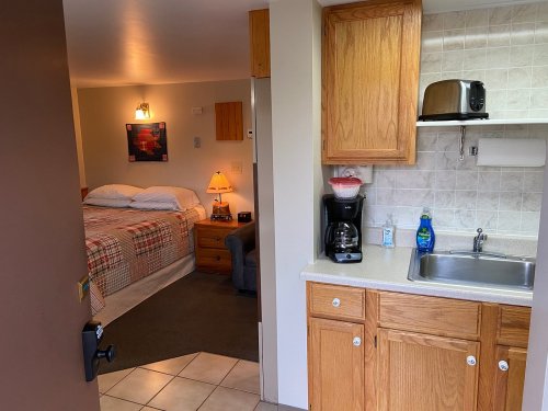 A view from a doorway into a small room with a bed and kitchenette, featuring a coffee maker and sink.