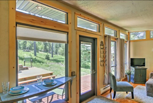 Bright interior of a modern living space with large windows, a dining area, and a view of a green outdoor landscape.