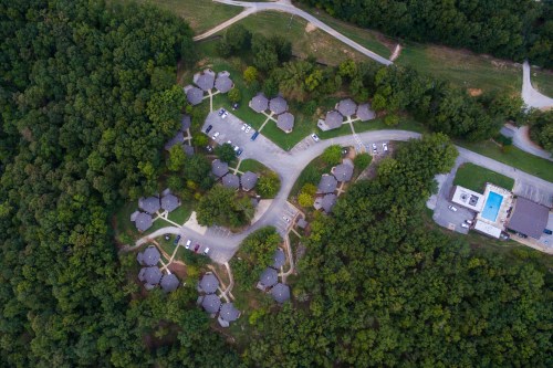 Aerial view of a cluster of homes surrounded by trees, with parking areas and a nearby building and pool.