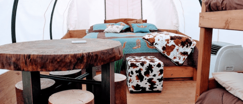 Cozy interior of a glamping tent featuring a bed, wooden table, and rustic decor with animal patterns.