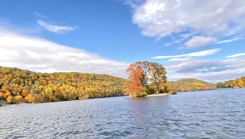 A serene lake surrounded by vibrant autumn foliage and a small island with colorful trees under a blue sky.