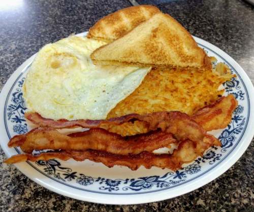 A plate of breakfast featuring toast, a fried egg, hash browns, and crispy bacon strips.