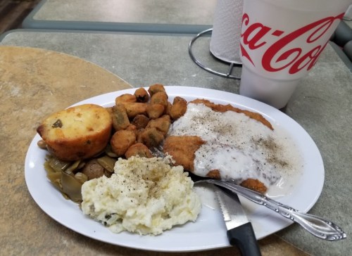 A plate of fried chicken with gravy, mashed potatoes, green beans, okra, cornbread, and a Coca-Cola drink.