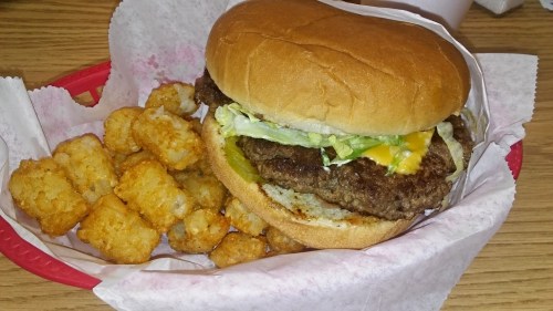 A juicy hamburger with lettuce and cheese, served with a side of crispy tater tots in a red basket.
