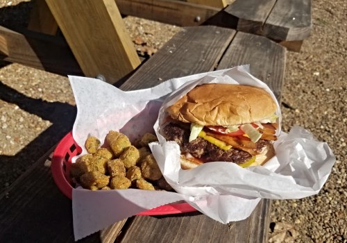 A juicy hamburger with toppings and a side of fried okra, served in a red basket on a wooden table.