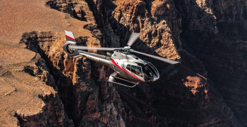A helicopter flying over a rugged canyon landscape, showcasing rocky cliffs and arid terrain below.