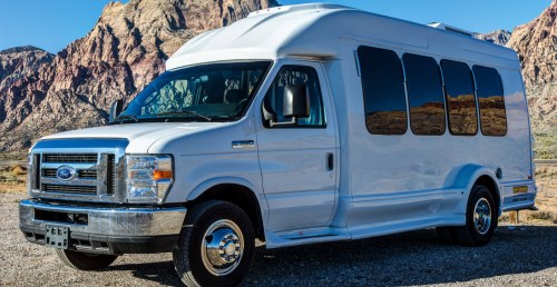 A white shuttle van parked in a scenic desert landscape with mountains in the background.