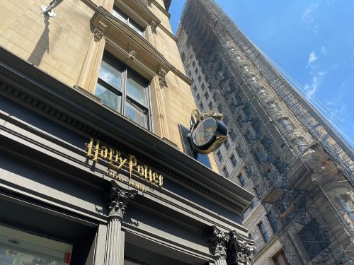 A building with a "Harry Potter" sign and a large clock, with scaffolding on a nearby structure under a blue sky.