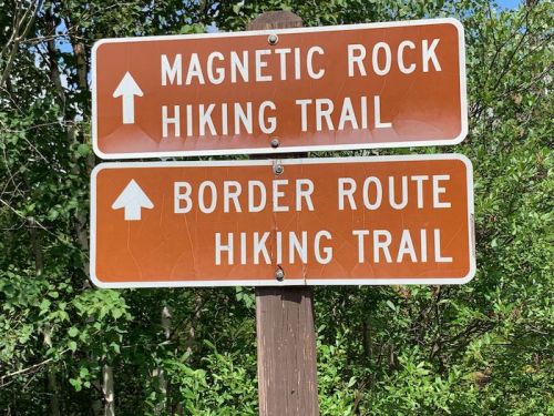 Two brown signs indicating hiking trails: "Magnetic Rock" and "Border Route," both with arrows pointing upward.