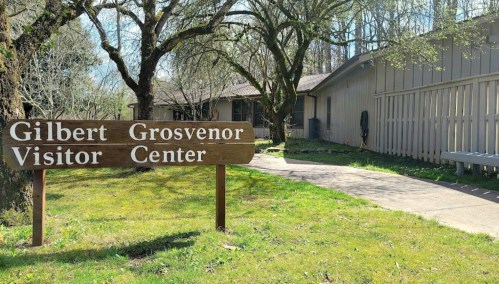 Sign for Gilbert Grosvenor Visitor Center in a grassy area with trees and a pathway leading to the building.