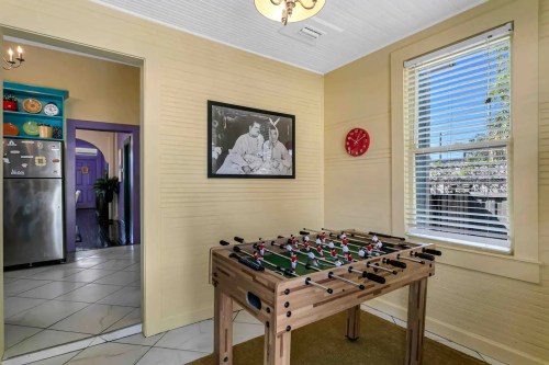 A cozy room featuring a foosball table, a wall clock, and a vintage photo, with bright windows letting in natural light.