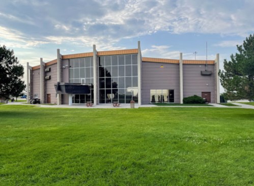 A modern building with large windows, surrounded by green grass and trees under a cloudy sky.