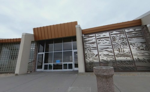 Entrance of a building featuring decorative metal panels and a glass door, set against a cloudy sky.
