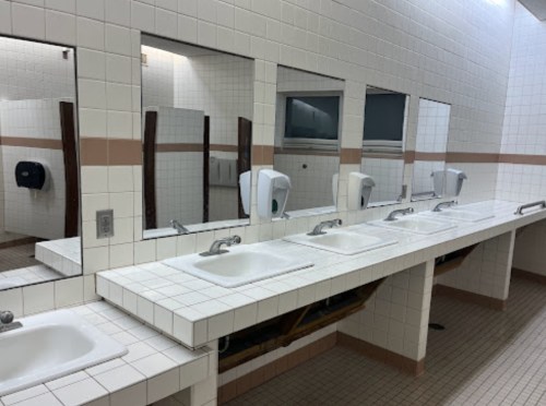 A clean public restroom with multiple sinks, mirrors, and soap dispensers against tiled walls.