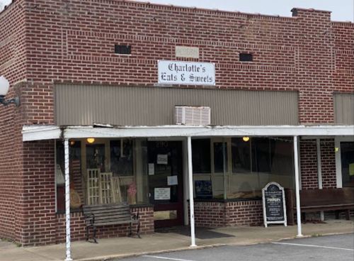 A brick storefront with a sign reading "Charlotte's Eats & Sweets" and a small outdoor seating area.