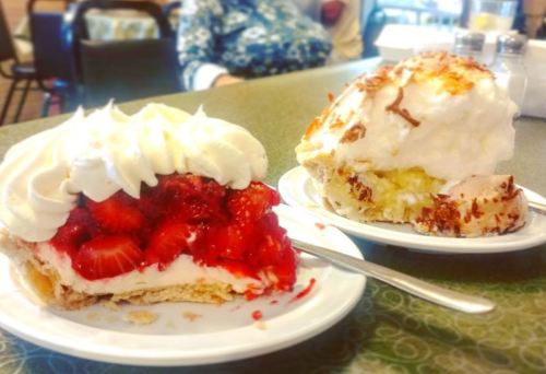 Two slices of dessert on white plates: one with strawberries and whipped cream, the other with coconut and cream.
