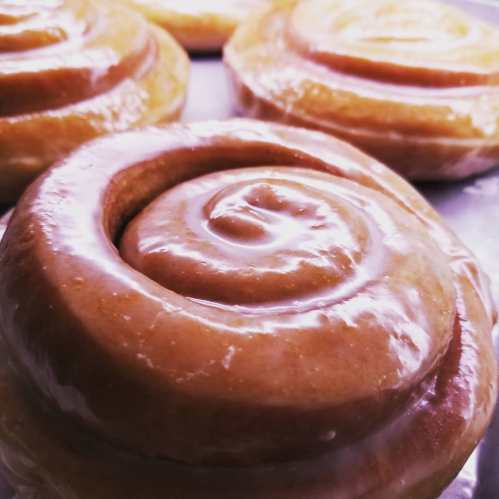 Close-up of glossy, spiral-shaped cinnamon rolls on a baking tray.