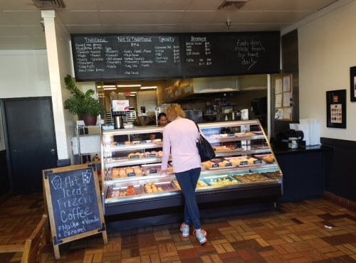 A customer browses a display case filled with pastries in a cozy café, with a menu board in the background.