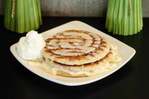 A plate with two large cinnamon rolls drizzled with icing, served with a dollop of whipped cream.