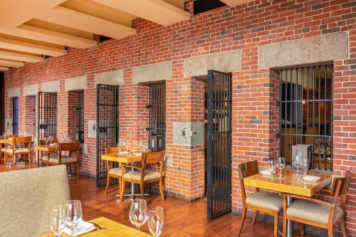 Interior of a restaurant featuring brick walls, barred windows, and wooden tables set for dining.