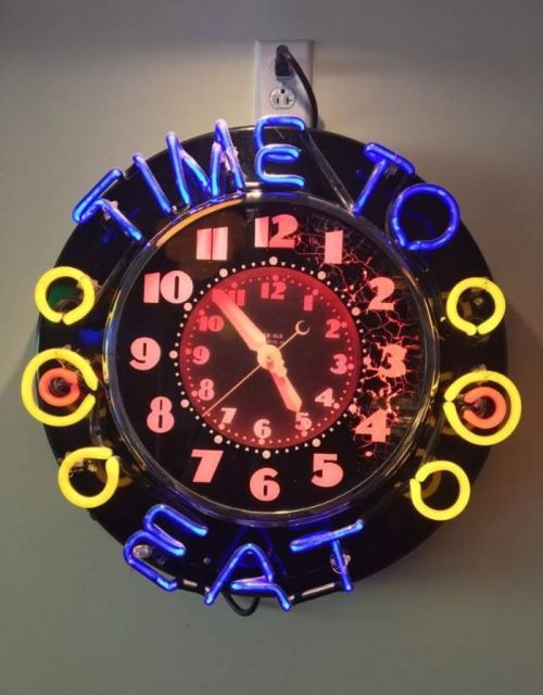 A round neon clock with the words "TIME TO EAT" illuminated, featuring colorful numbers and a black background.