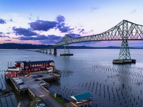 A scenic view of a bridge over water at sunset, with a restaurant and parking area in the foreground.