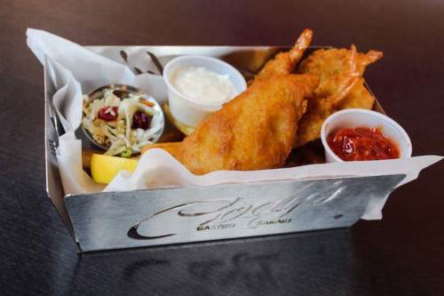 A metal tray holds two golden fried fish fillets, coleslaw, and dipping sauces.