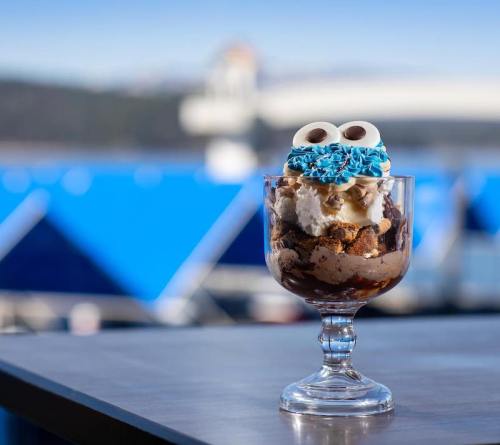 A dessert glass filled with layers of chocolate, whipped cream, and blue sprinkles, set against a scenic outdoor backdrop.