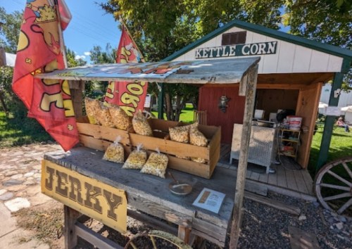 A rustic stand selling kettle corn and jerky, with colorful flags and bags of popcorn displayed outside.