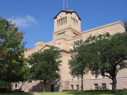 Historic building with a clock tower, surrounded by trees and a clear blue sky.