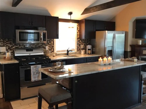 Modern kitchen with dark cabinets, stainless steel appliances, a marble countertop, and candles on the island.
