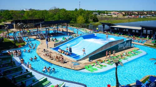 A vibrant water park scene featuring a wave pool, sunbathers, and a lazy river surrounded by greenery.
