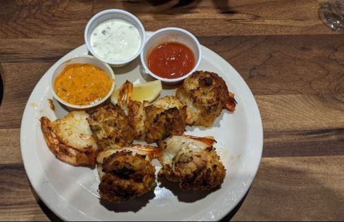 A plate of fried shrimp with three dipping sauces: orange, white, and red, served with a lemon wedge.