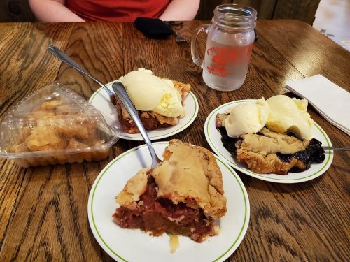 Three plates of pie with ice cream, a container of cookies, and a glass of water on a wooden table.