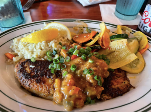 A plate of blackened fish topped with a colorful sauce, served with rice and sautéed vegetables, garnished with lemon.