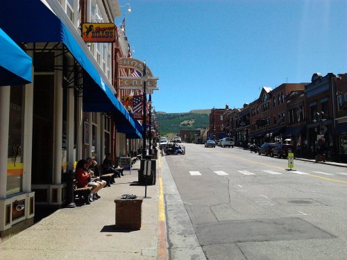 A sunny street scene with shops, benches, and mountains in the background, showcasing a vibrant small-town atmosphere.
