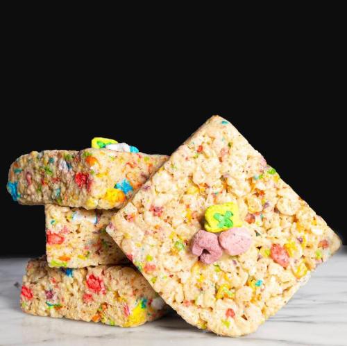 Four colorful rice cereal treats stacked on a marble surface, featuring bright sprinkles and shaped marshmallows.
