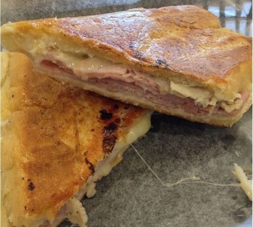 A golden-brown sandwich cut in half, revealing layers of ham and melted cheese inside.